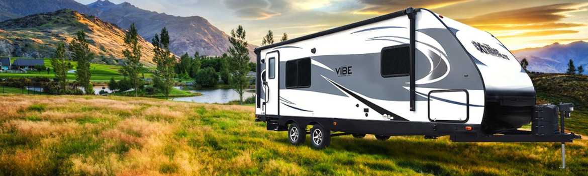 A 2018 Forest River Vibe Extreme Lite 258RKS parked on a grassy hill with scenic mountains and forest in the background.